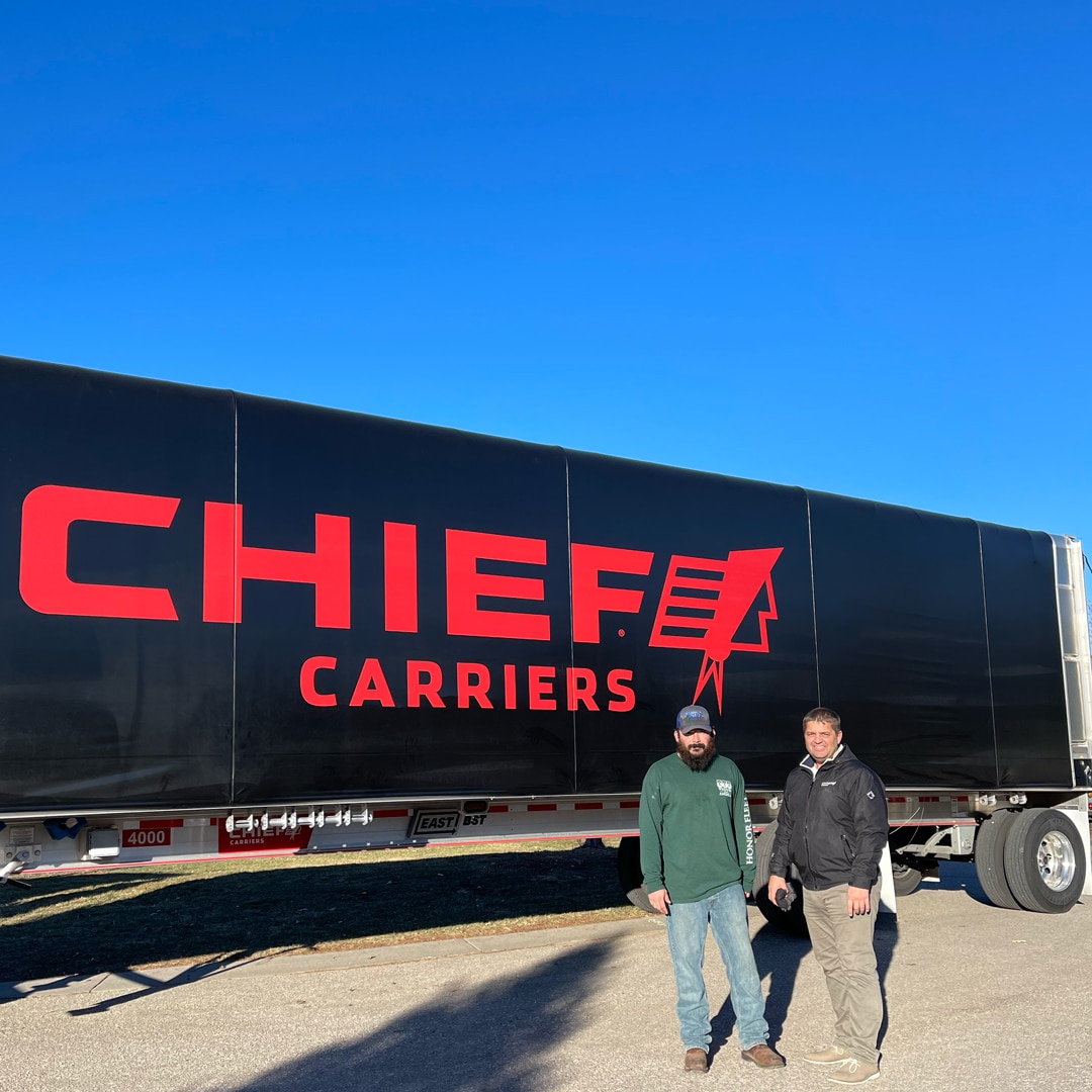 two truck drivers in front of a chief carriers trailer