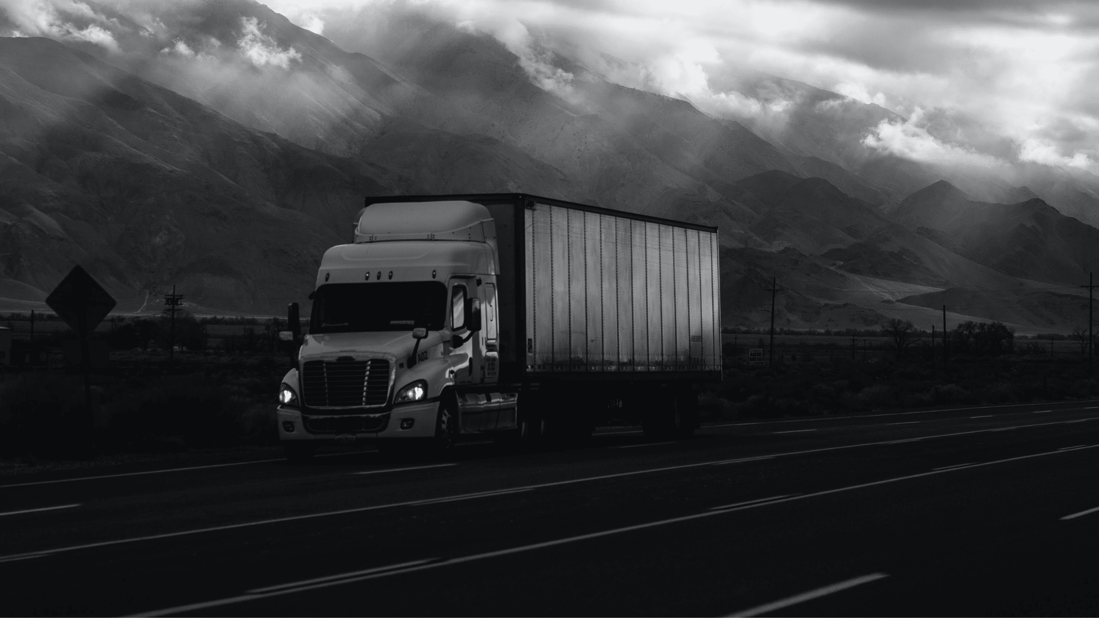a white semi truck and trailer driving in front of mountains on a highway