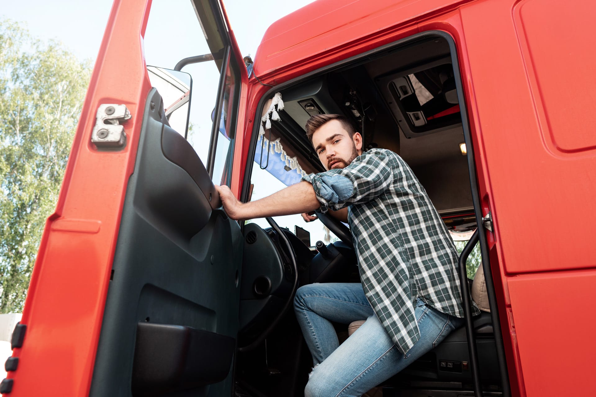 Handsome bearded truck driver from gen z inside his red cargo truck