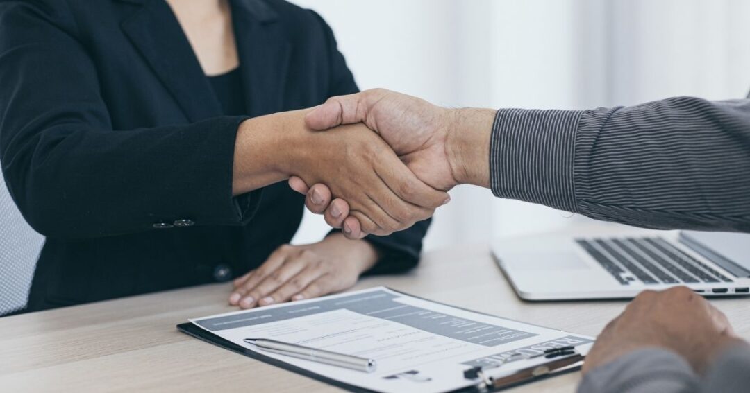 Two people shaking hands in an interview setting.