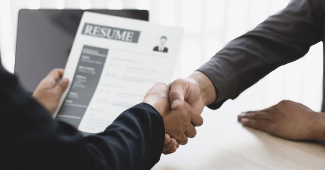 Two people shaking hands, one holding a resume document