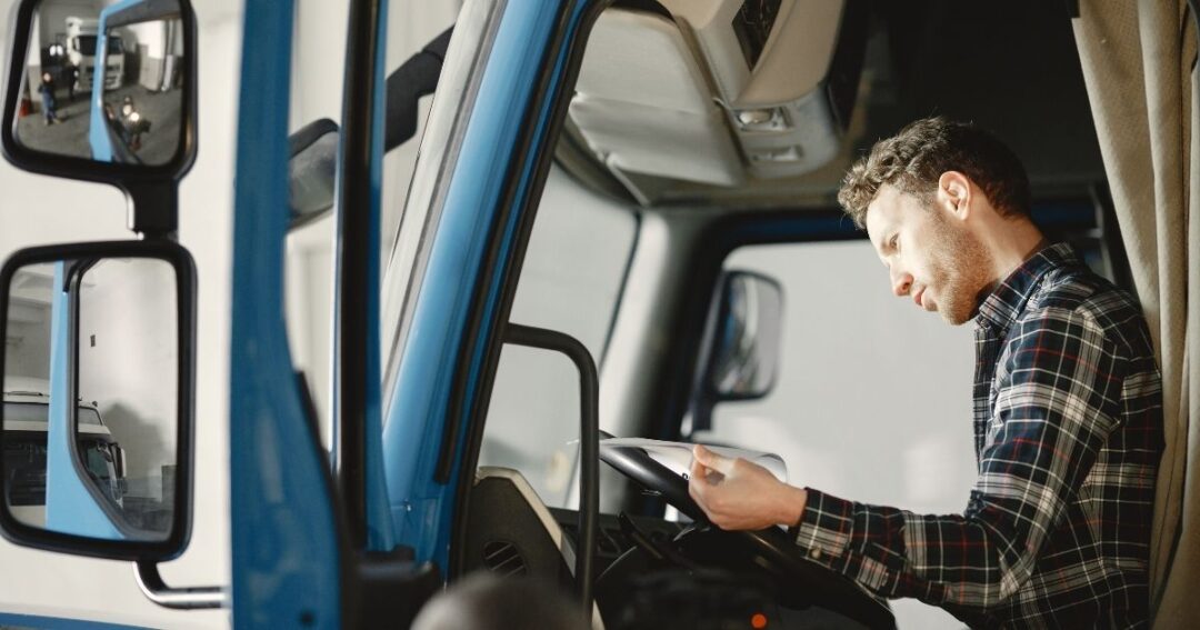 Male truck driver reading paperwork in the a semi-truck cab