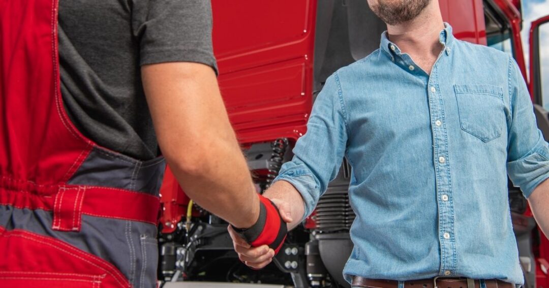 Two men standing by a semi-truck shaking hands