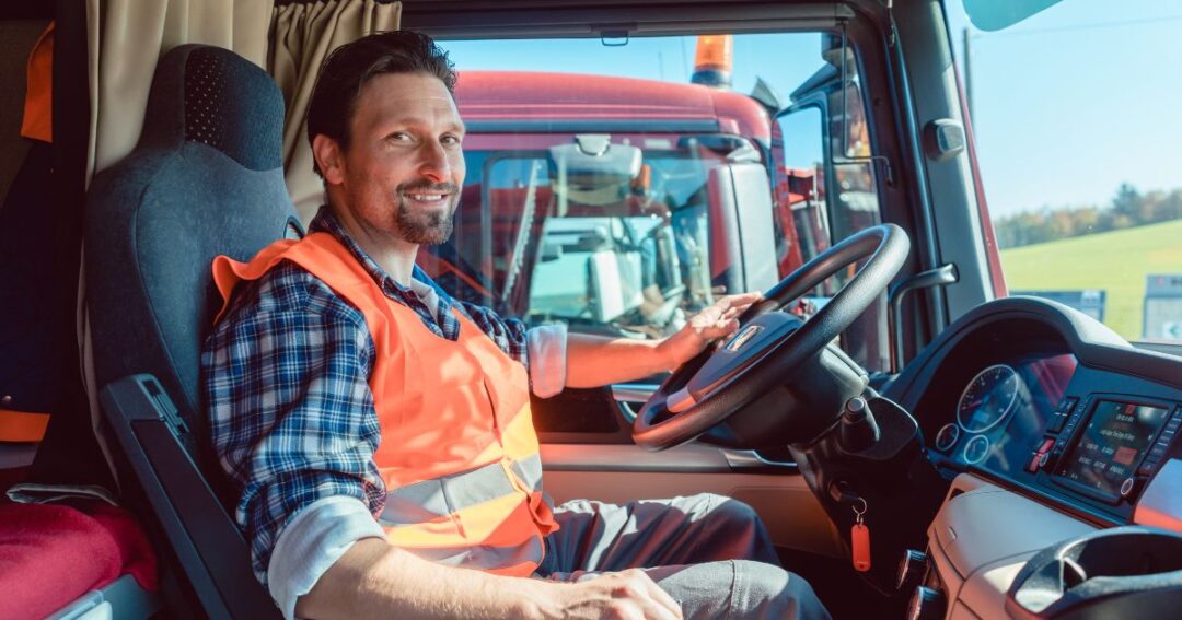 Smiling truck driver behind the wheel of a semi-truck.