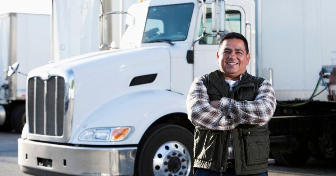 Smiling male truck driver in front of semi-truck.