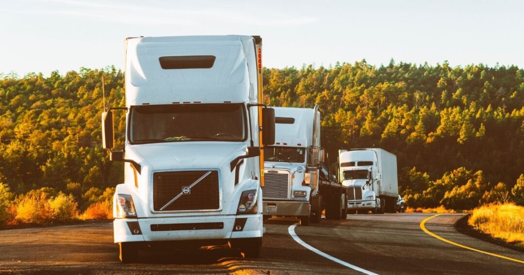 Three semi-trucks on a rural highway.