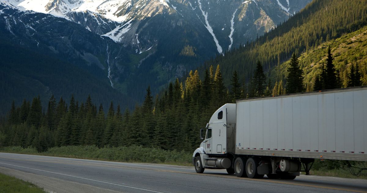 A white semi-truck driving through the mountains.