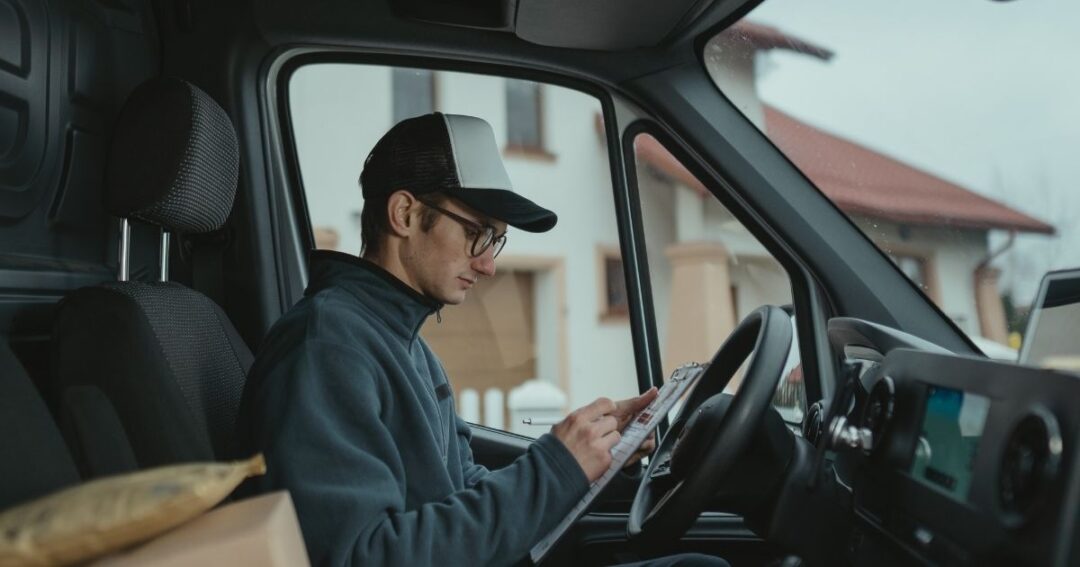 A driver is checking paperwork on a clipboard.