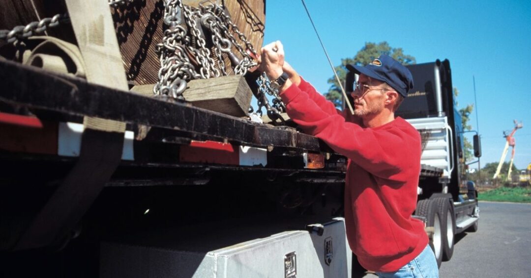 Driver checking chain tension for a flatbed load he is hauling.