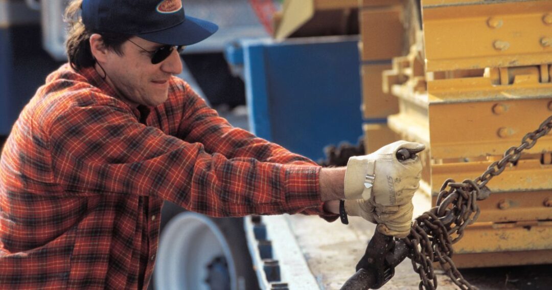 Driver tightening chains for flatbed load securement safety and compliance.