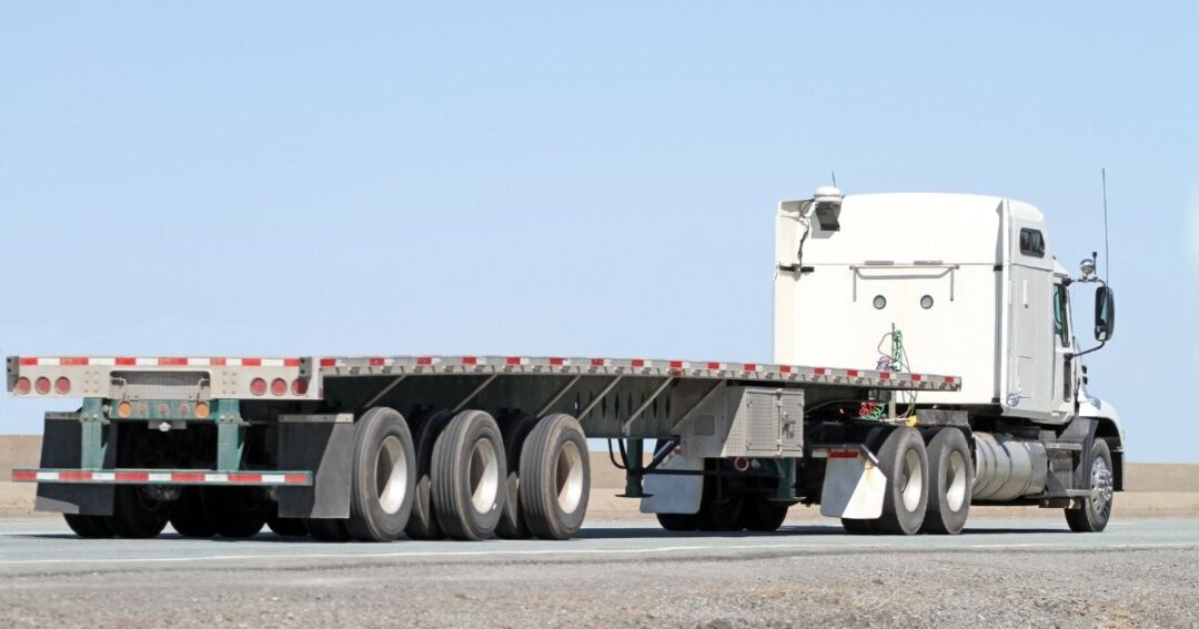 An empty flatbed truck on a highway.