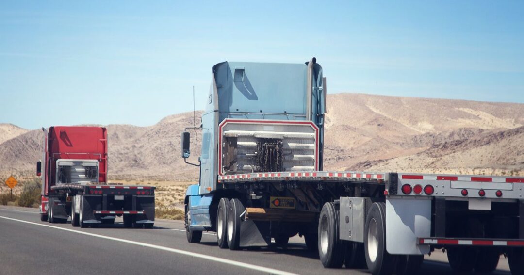 Two empty flatbed trucks on a highway road.