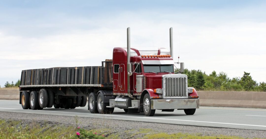Efficient load planning is an effective freight cost reduction strategy. A red flatbed truck hauling a load on a highway.