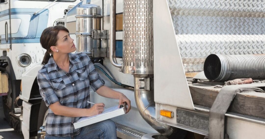Woman with clipboard inspecting a flatbed truck.