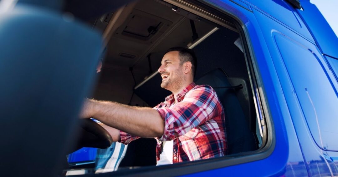 Smiling truck driver behind the wheel of a semi-truck.