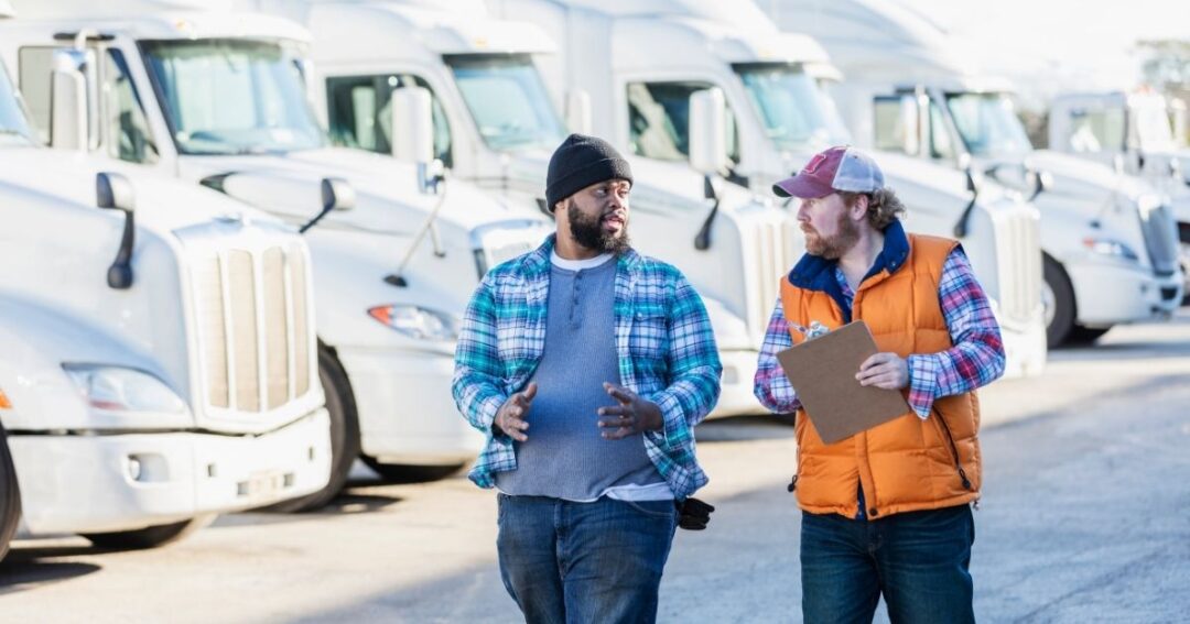 Two trucker drivers talking, parked semis in the background.