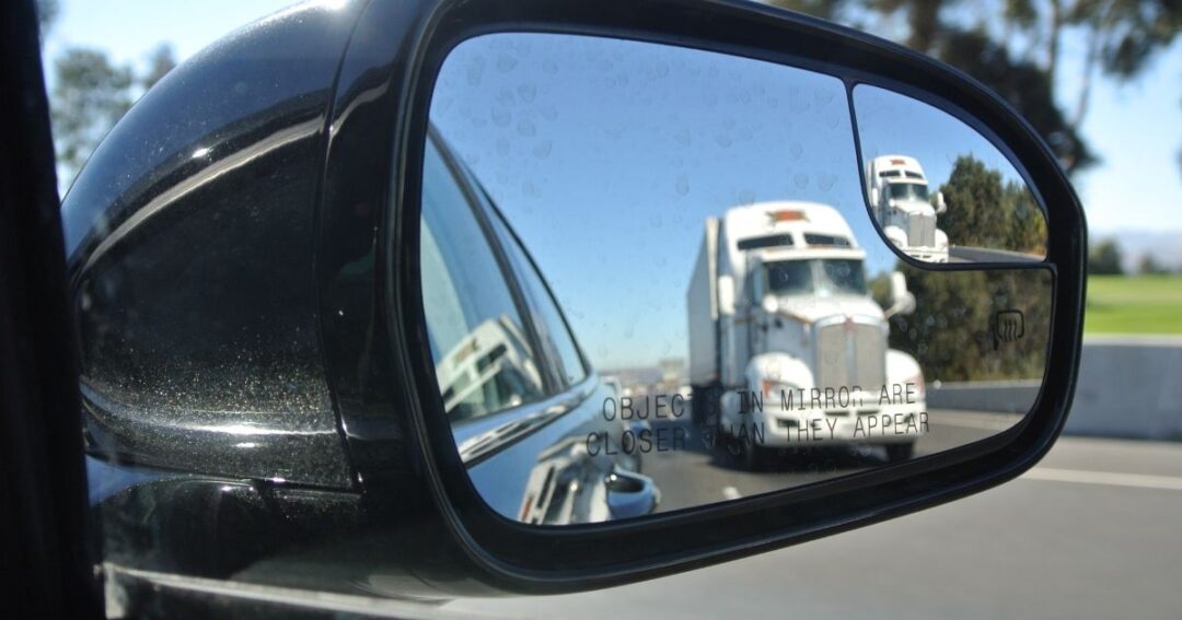 Reflection of a semi-truck in a car side mirror.