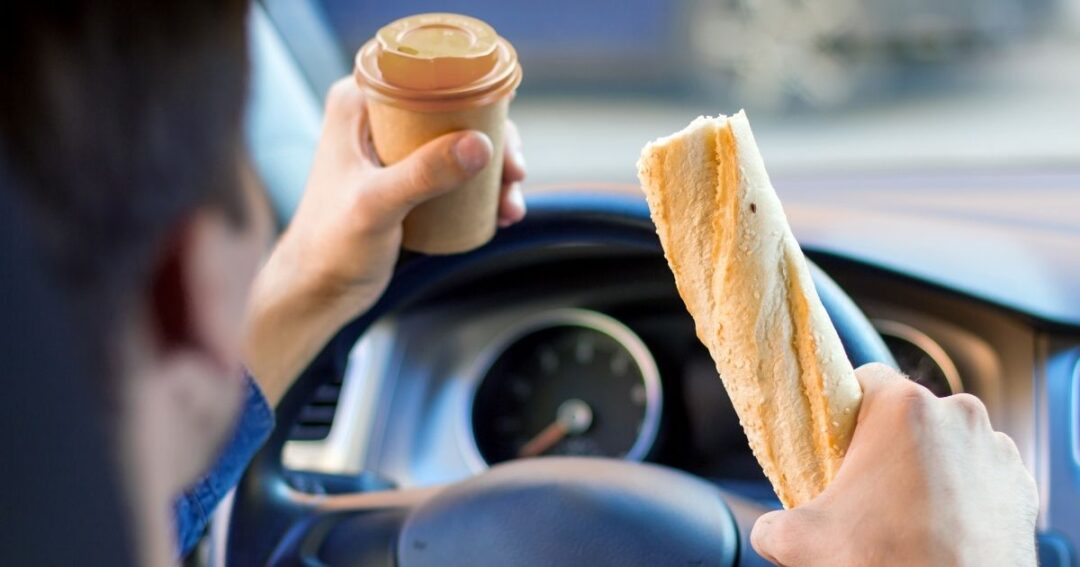 A driver is holding food and drink while driving.