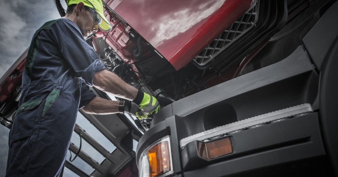 Low-angle view of a semi truck technician working on an engine.