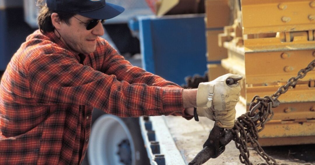 Man tightening chains to secure cargo for flatbed shipping.