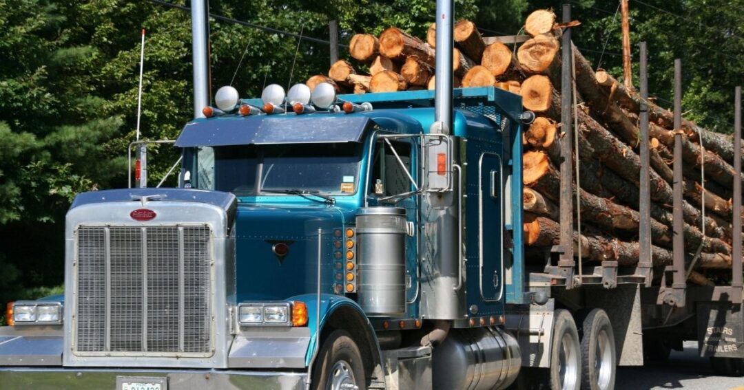 A blue flatbed truck hauling a load of logs.