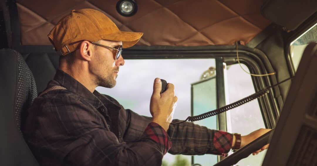 A male truck driver on the radio in the truck cab.