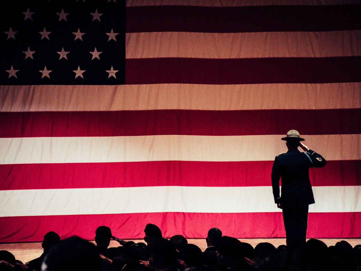 Military servicemembers saluting a large flag