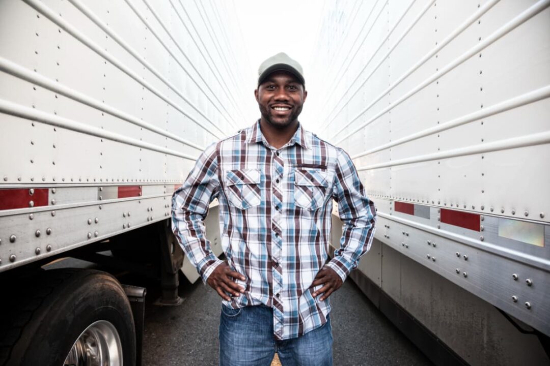 Smiling, healthy truck driver standing in between two trucks.