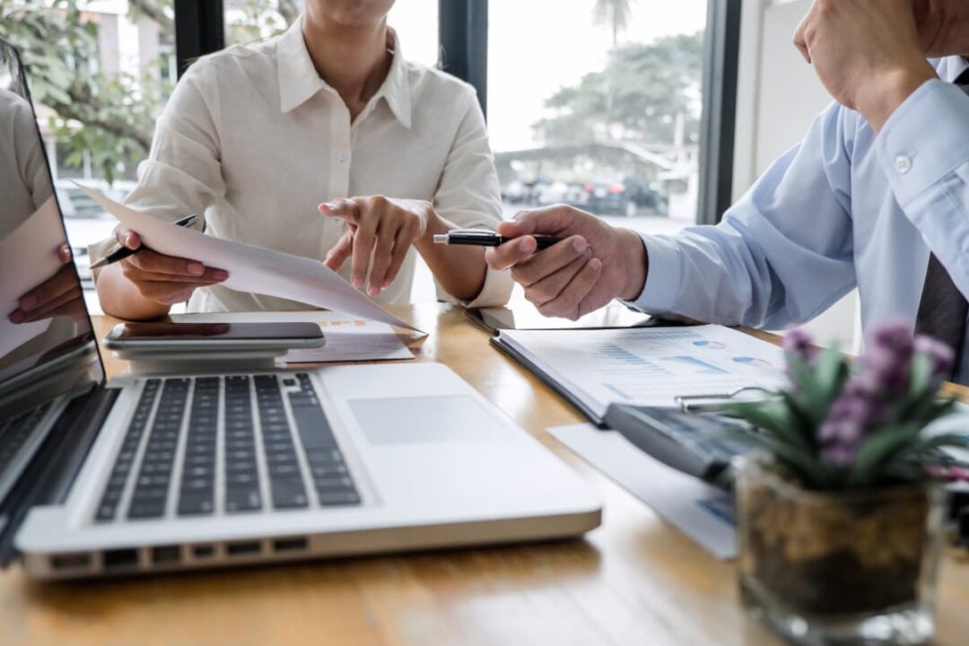 Unidentified man and woman looking over paperwork and laptop information in a business meeting.