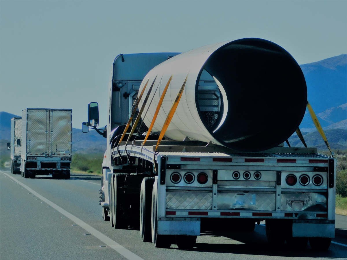 A flatbed truck transporting a very large cylinder by highway.