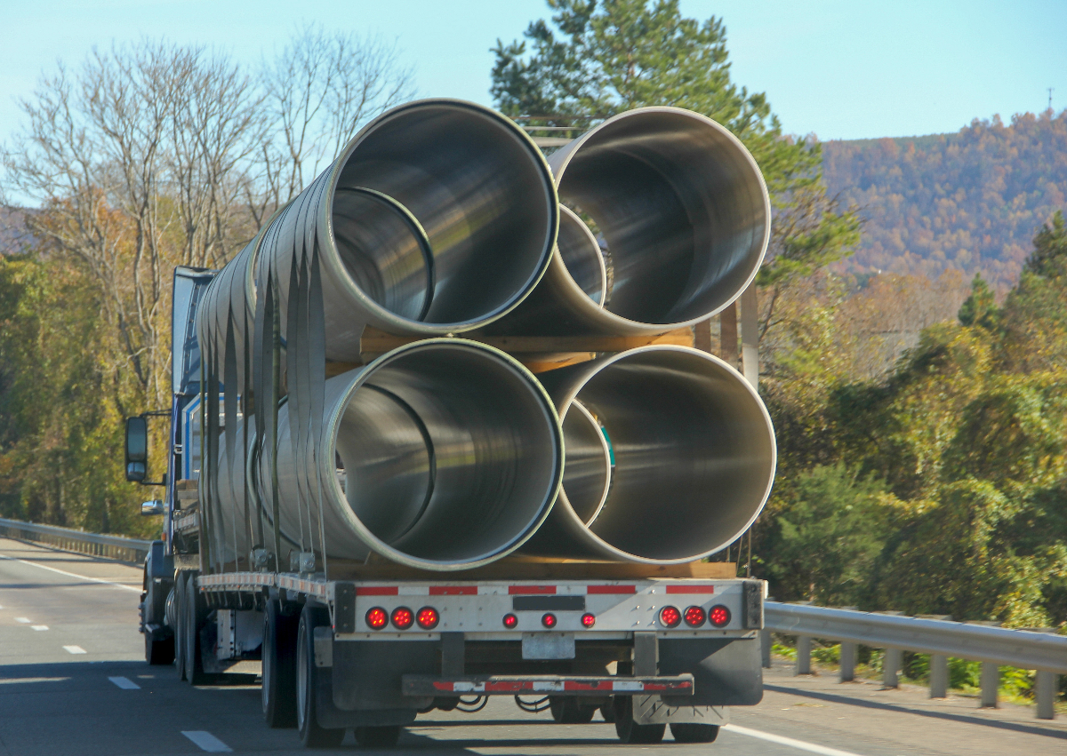 An oversized flatbed load of large metal cylinders being transported by highway.