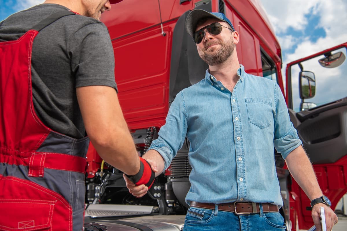 A truck driver shaking hands with a mechanic.