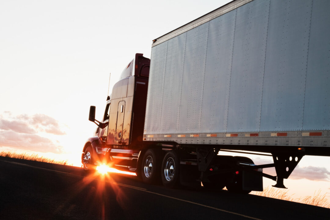 A semi truck backlit by the sun.