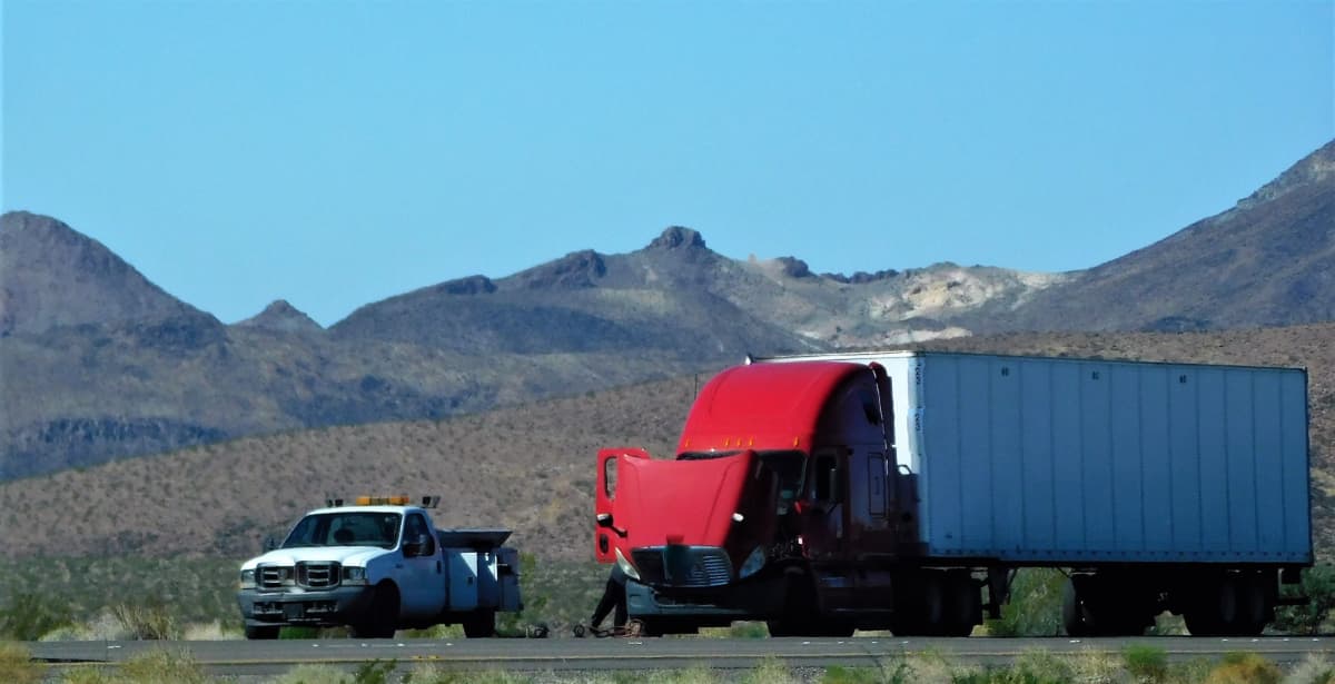 A mobile roadside service technician working on a semi truck on the side of a highway.
