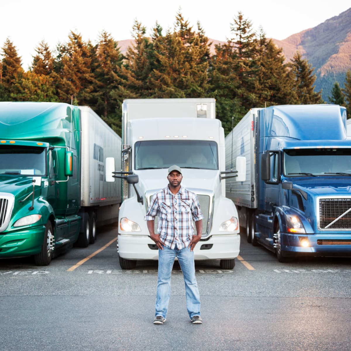 A young male truck driver standing in front of parked semi trucks.