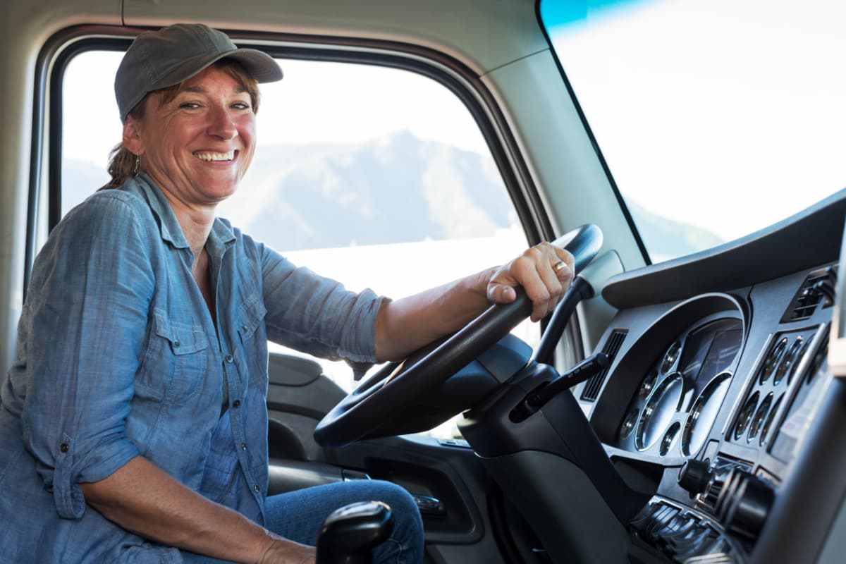A smiling female truck driver behind the wheel of a semi truck.
