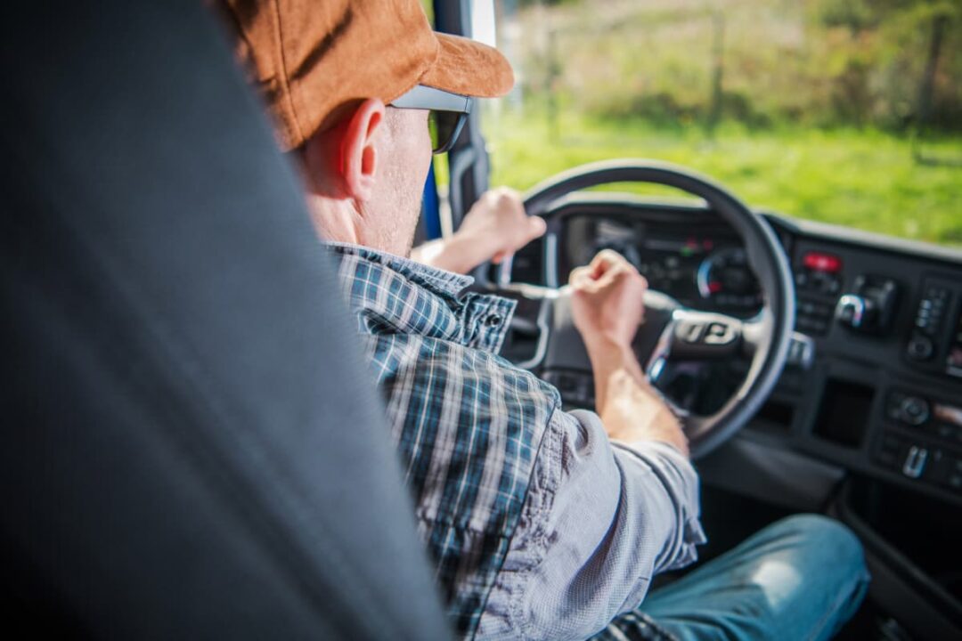 Male truck driver behind the wheel of a commercial truck.