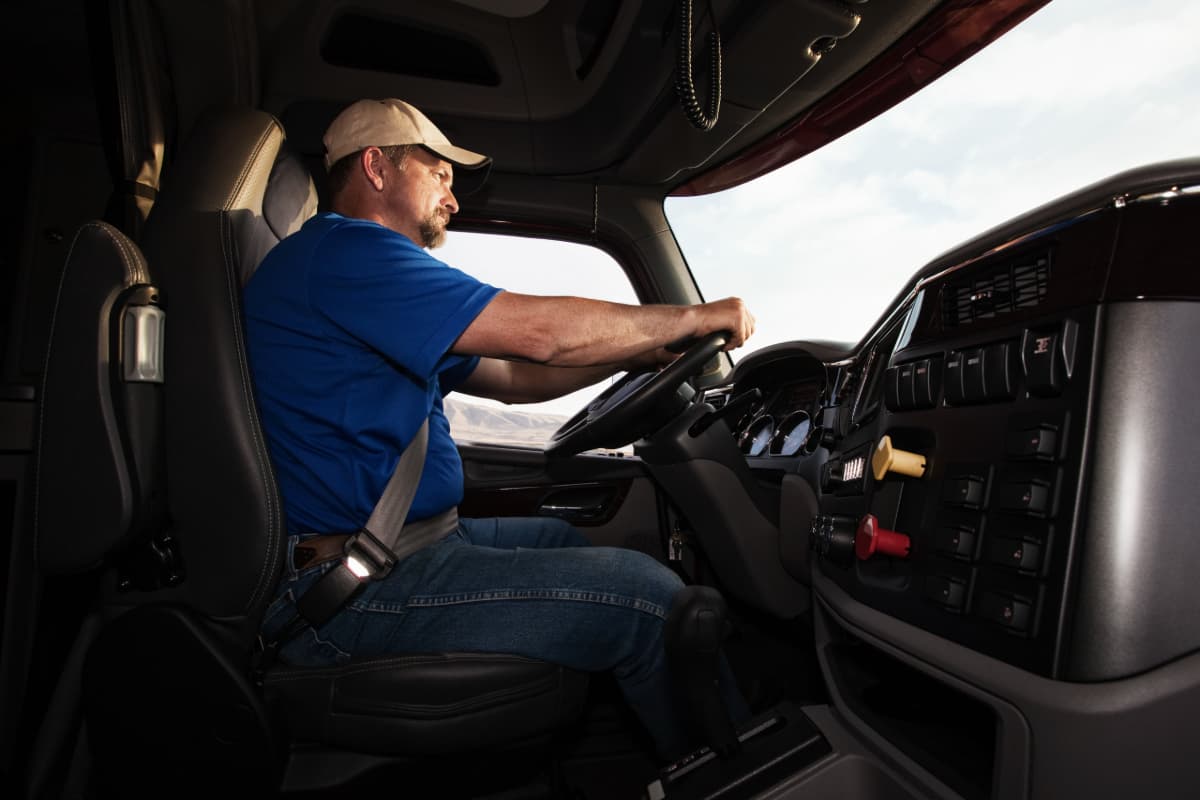 A male truck driver behind the wheel of a semi truck.