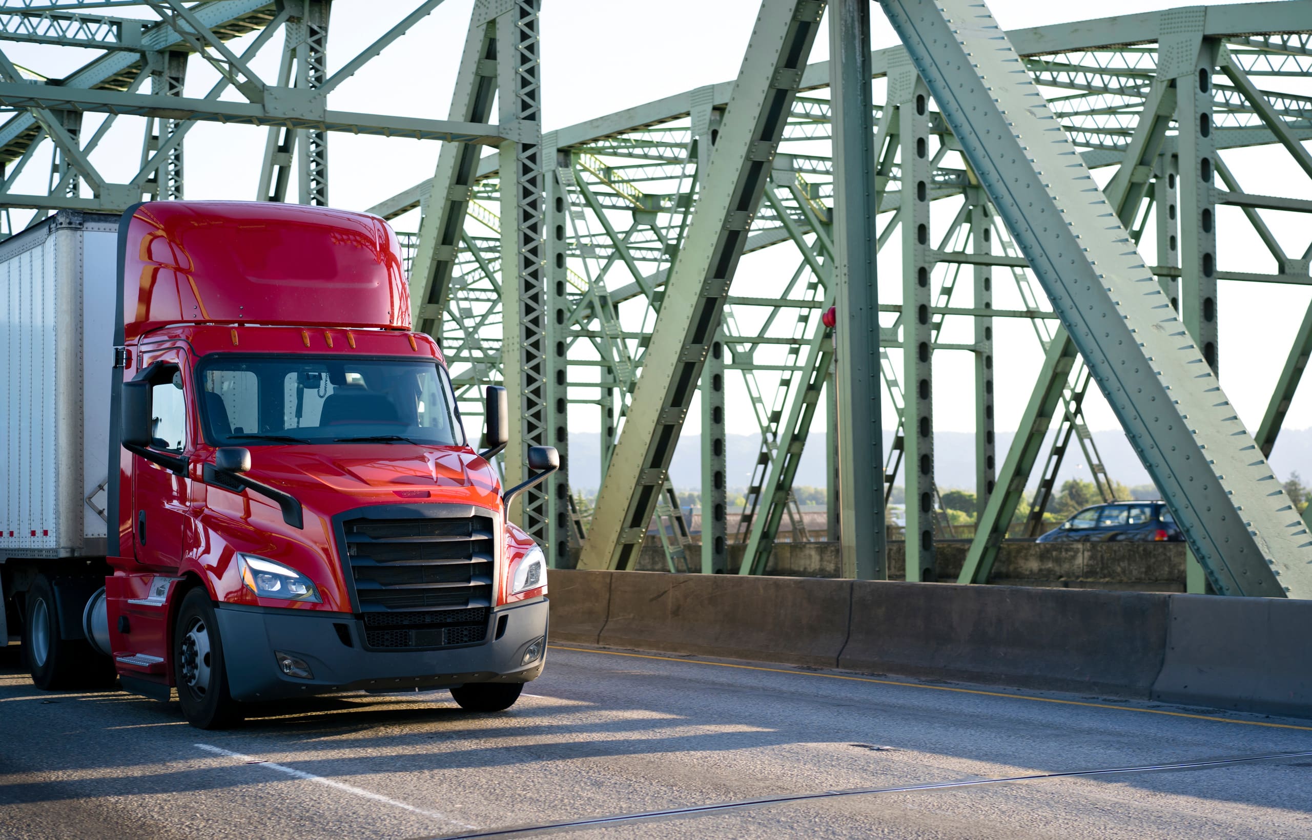 Bonnet red big rig day cab semi truck transporting cargo in dry van semi trailer driving on the truss bridge
